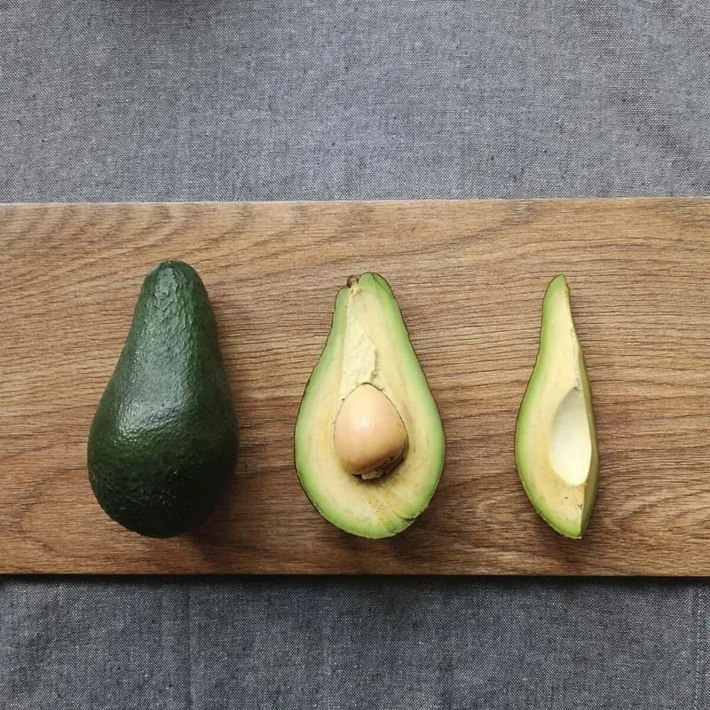 Ganze, halbe und aufgeschnittene Avocado in einer Reihe auf einem Holzbrett
