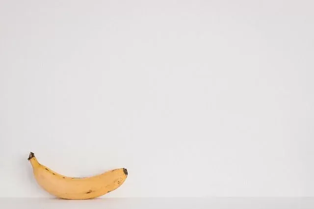 Eine reife Banane mit braunen Flecken vor einer schlichten weißen Wand
