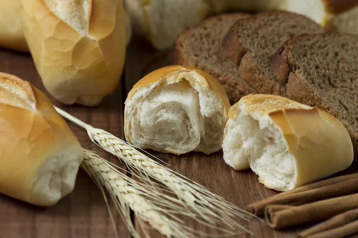 Weiße Brötchen, dunkles Schnittbrot, Weizenähren und Zimtstangen auf Holz