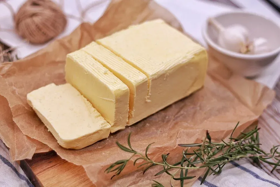 In Scheiben geschnittener Butterblock auf Backpapier neben einem Rosmarinzweig