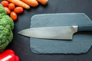 Couteau de chef posé sur une ardoise, avec brocoli, tomates et carottes