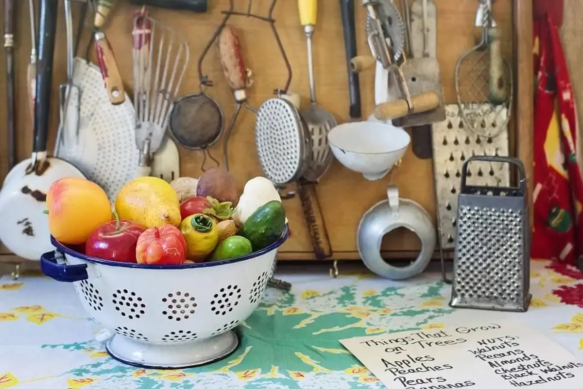 Passoire émaillée remplie de fruits devant d'anciens ustensiles accrochés