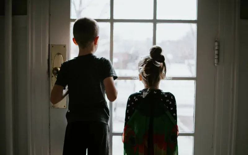 Two children in costumes looking out of a glass front door