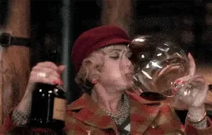 Femme en manteau rouge et béret buvant du vin dans un très grand verre