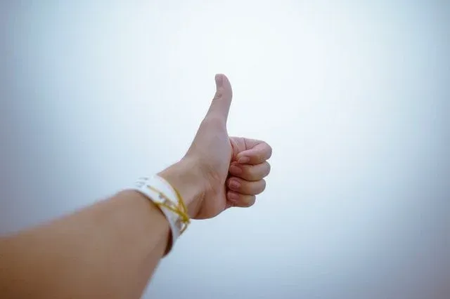 Main levée avec le pouce en l'air, bracelets au poignet