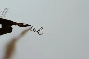 A fountain pen writing the word ink on a blank sheet of paper