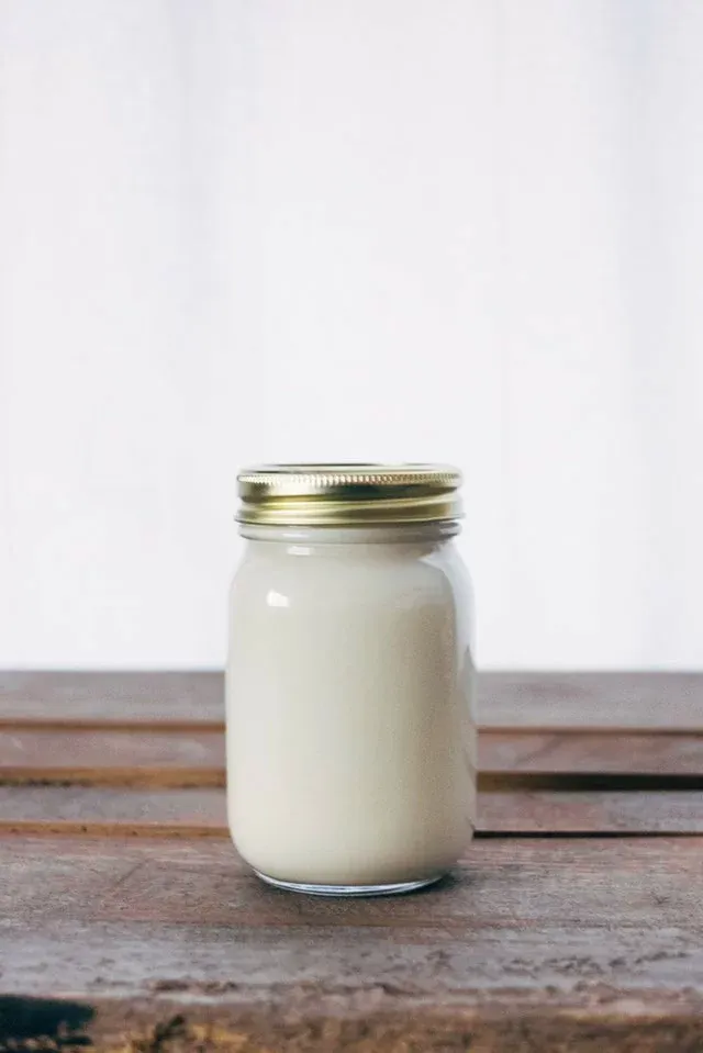 Słoik z białym napojem i złotą zakrętką na drewnianym stole