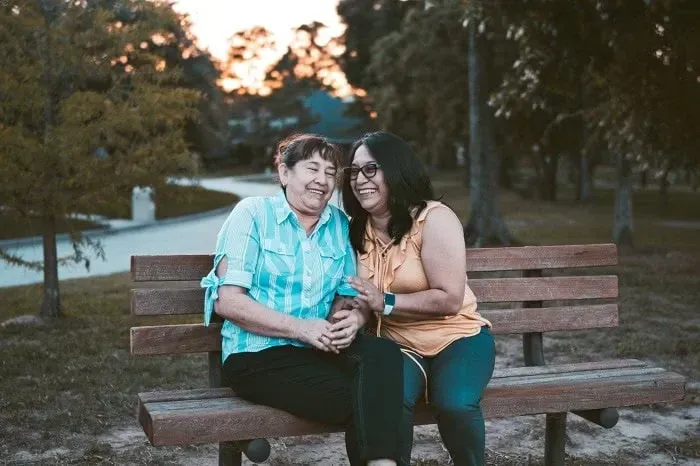 An older woman and a younger woman laughing together on a park bench at dusk
