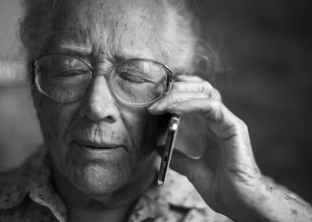 Black-and-white close-up of an older woman in glasses talking on a mobile phone