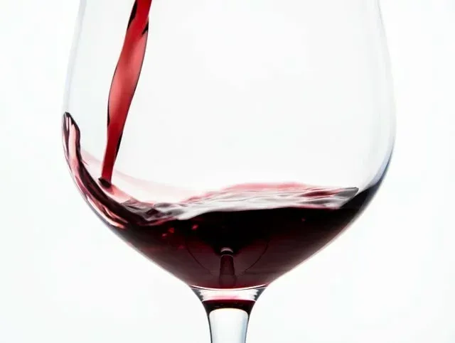 Czerwone wino wlewane do kieliszka na białym tle